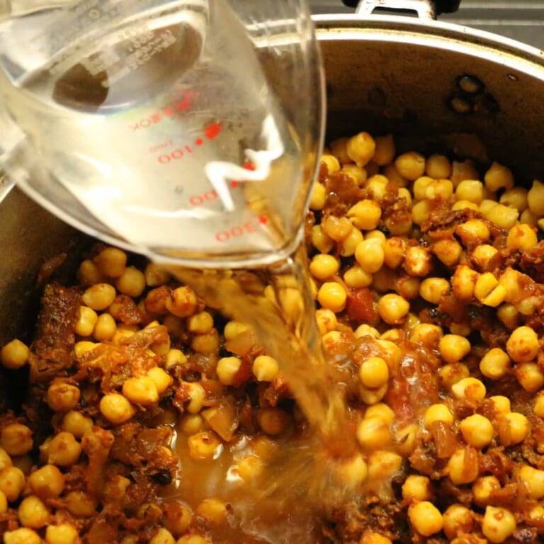 手順 7: ざるにあげたひよこ豆を加えて混ぜ合わせた後、水(約200ml)を加え、蓋をして約10分ほど煮込みます。
