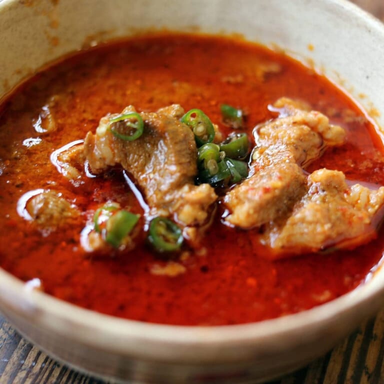 青唐辛子をのせた真っ赤な豚肉のヴィンダルーカレーの器のアップ