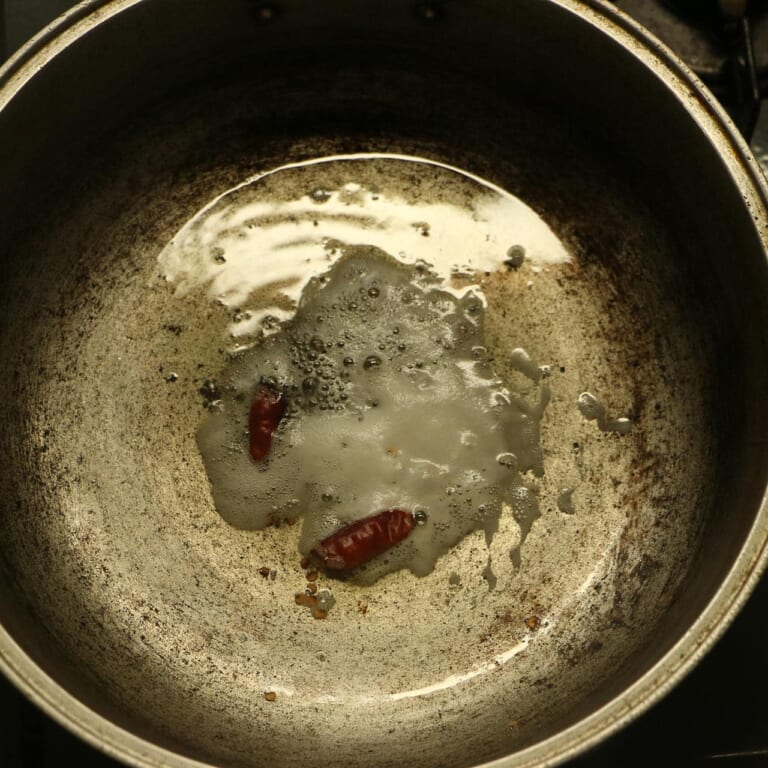 手順 1: 温めたフライパンに油をひき、スパイスA（マスタードシード、レッドペッパー）を加えます。