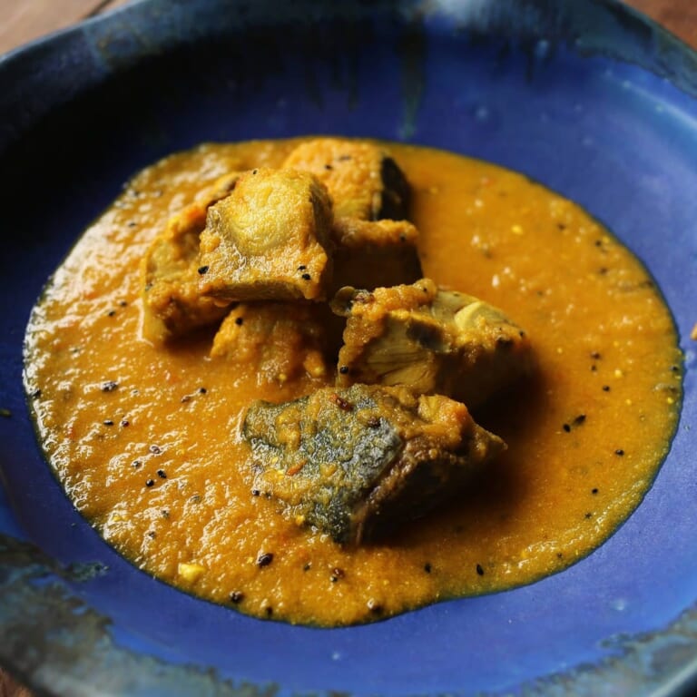 青い皿に盛られたベンガル料理の象徴マスタード香る魚カレー、鮮やかな黄金色のグレービー