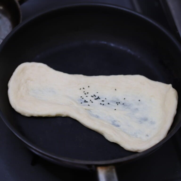 手順 6: フライパンを熱して伸ばした生地をおき、カロンジを5、6粒ふりかけ蓋をして焼き色がつくまで４、5分焼く。