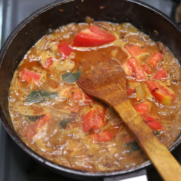 手順 4: 水を少しずつ加えていき、グツグツしてきたらトマトとカレーリーフ 、青唐辛子を加える。