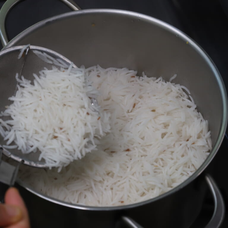 手順 5: 茹でたバスマティライスをザルなどであけ、敷き詰めた鶏肉の上に被せていく。