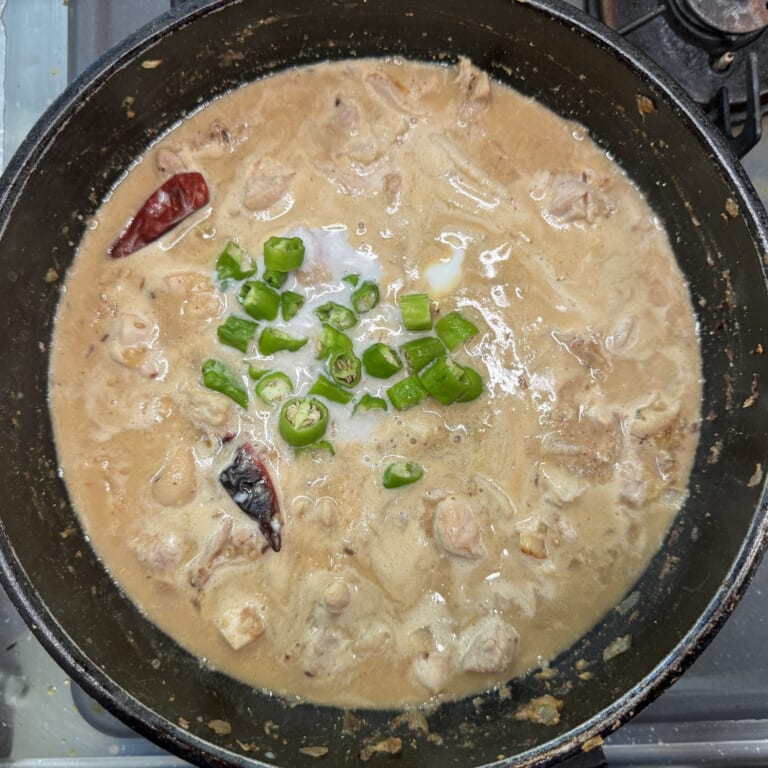 手順 5: 水を少しずつ加えて伸ばし、蓋をして１５分ほど煮込む。鶏もも肉に火が通ったらココナッツミルク、ししとうを加え、一煮立ちさせ