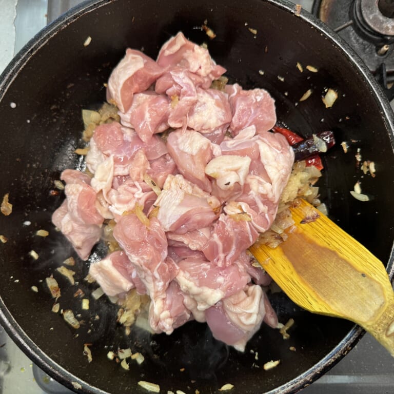 手順 3: 玉ねぎがほんのり色づいたらすりおろしたにんにく、生姜、鶏もも肉を加えて炒める。