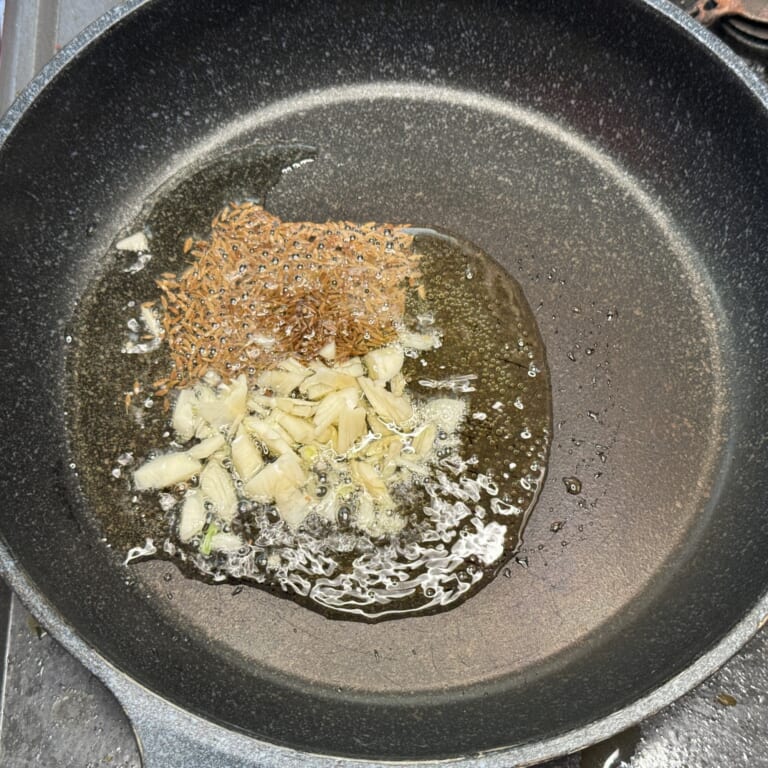 手順 6: 別のフライパンにギー（仕上げ用）を加え、スパイスCを熱しみじん切りにしたにんにくを熱する。