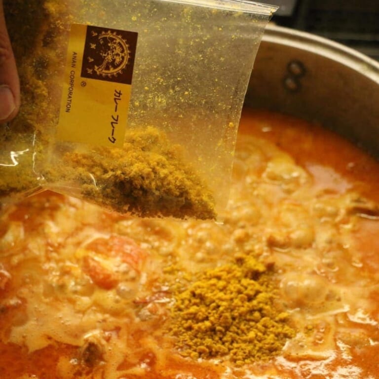 手順 4: トマトの形がくずれてきたら少しずつ水で伸ばし、カレーフレーク(半量)を加える。