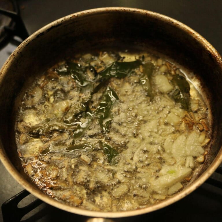 手順 3: 別のフライパンに油をひき、マスタードシード、にんにく、カレーリーフを加える。パチパチしてきたら、油ごと一気に鍋に加えて完