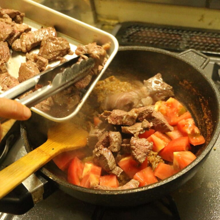 手順 6: 取り出しておいた牛肉、トマトを加え炒めあわせ水を少しずつ加えていく。