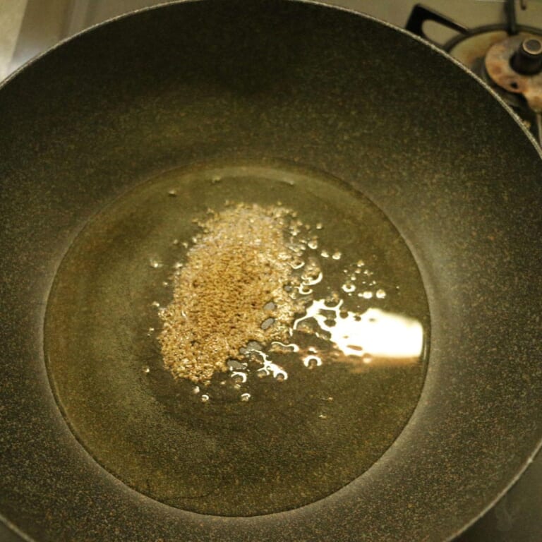 手順 2: 温めた油を入れた鍋にスパイスA(アジョワン)を入れ、玉ねぎを加えます。