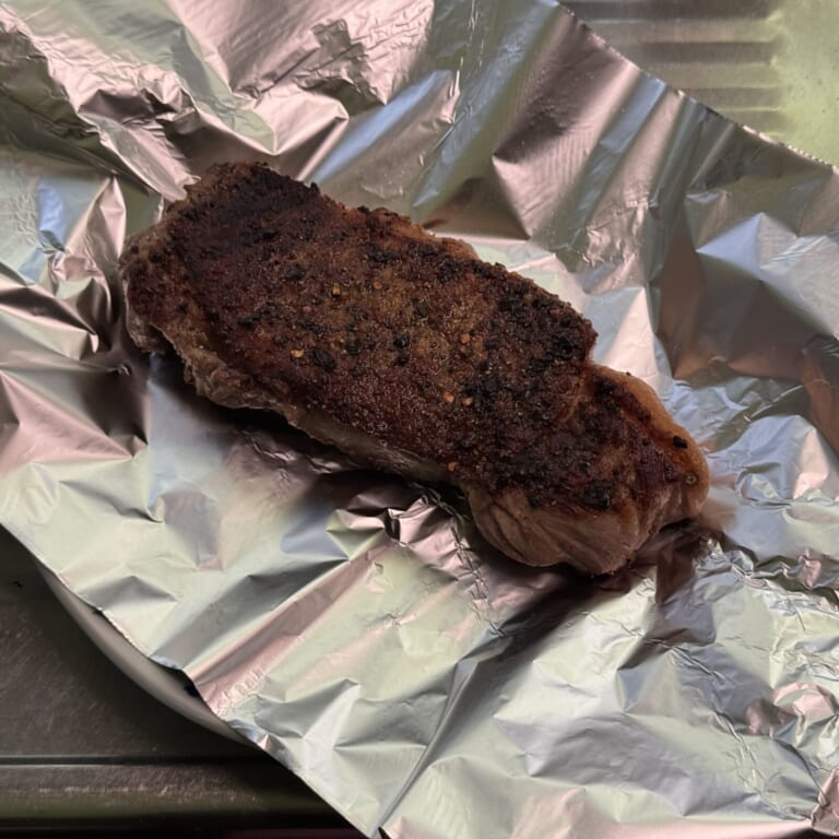 手順 3: ステーキ肉を取り出し、アルミホイルとタオルに包み、温めたお皿に乗せて5分から10分程度寝かせる。寝かせた後、カットして盛