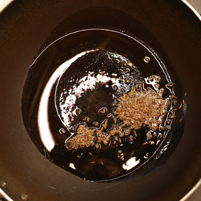 工程 2: フライパンに油とクミンシードを入れて熱し、テンパリングする様子