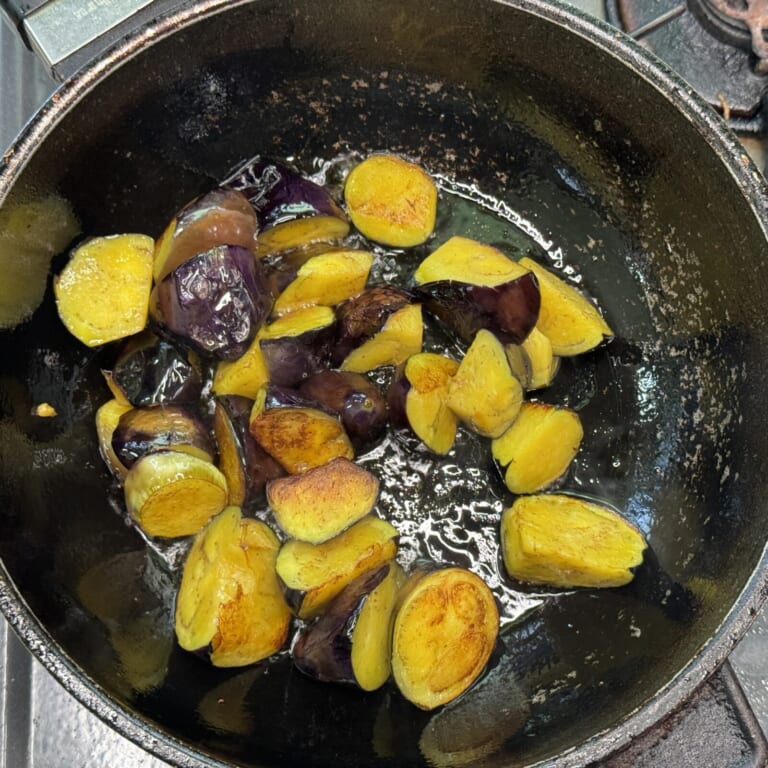 手順 2: 温めたフライパンに油（マスタードオイル）を加えナスの表面を焼くように炒める。