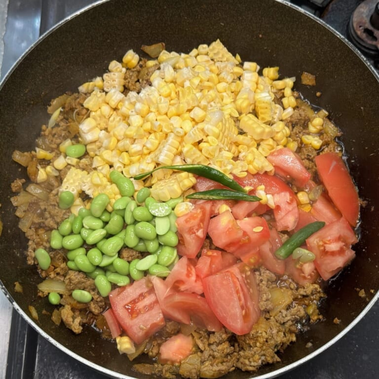 手順 3: 豚ひき肉を加えしっかりと火が通るまで炒める。枝豆、トウモロコシ、トマト、青唐辛子を加え軽く炒め合わせたら蓋をして10分ほ