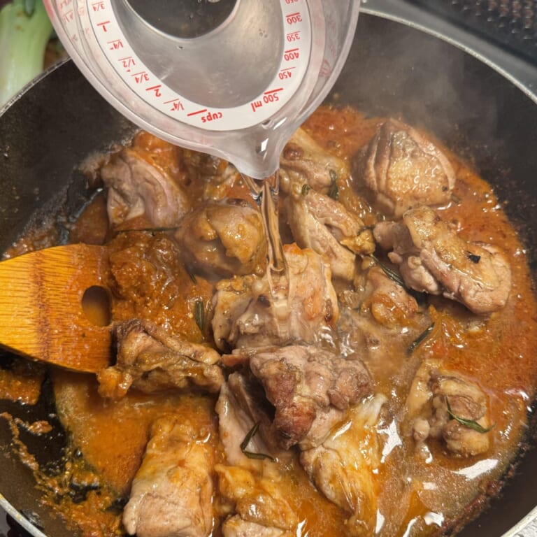 手順 6: 鶏もも肉を鍋に戻し水を少しずつ加え一緒に煮込み、ぐつぐつとしてきたら弱火にして蓋をして弱火で5分熱する。表面に油が浮いて
