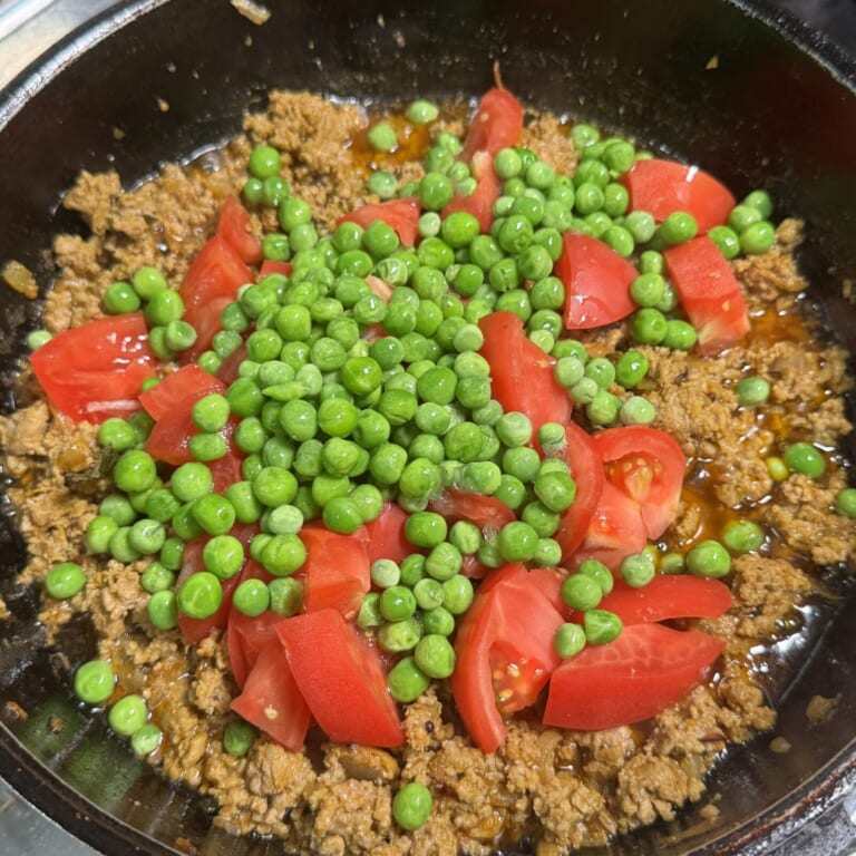 手順 5: トマトとグリーンピースを加え鍋に蓋をして弱火にして約10分煮込む。