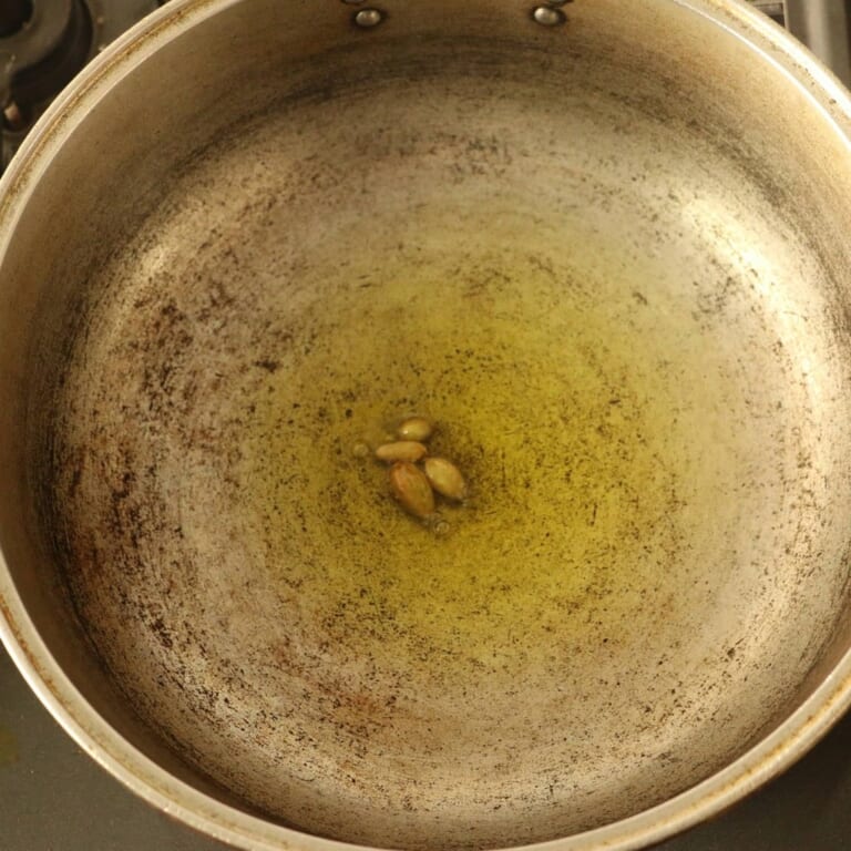 手順 1: 温めたフライパンでサラダ油を熱し、スパイスA（カルダモン）を加えます。